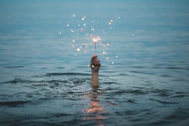 Photo of hand emerging from water with sparkler by Kristopher Roller on Unsplash